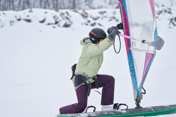 A middle-aged woman, a snowsurfer, rides a sailboard. Snowsurfing on a cloudy winter day.