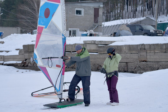 A middle-aged man and woman, snowsurfers, prepare sailboards for skiing in the snow. Preparing to ride a sailboard in the snow on a cloudy winter day.