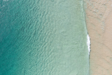 Aerial view of a beach with gentle waves and white sand in a tropical wonderland