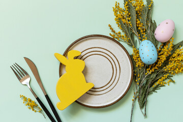 Easter table setting. Plate with easter eggs and mimosa on a pastel green background. Happy Easter...