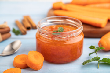 Carrot jam with cinnamon in glass jar on blue wooden. Side view, selective focus.