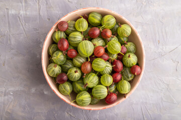 Fresh red and green gooseberry in ceramic bowl on gray concrete, top view.