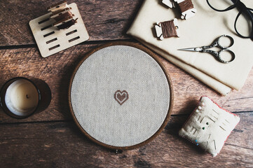 cross stitch embroidery accessories. Linen cloth in hoop, scissors, cloth and floss on wooden background. Indoor hobby concept. - obrazy, fototapety, plakaty