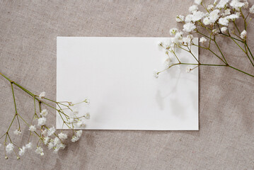 Blank paper card and gypsophila flowers on neutral beige linen texture background, aesthetic floral...