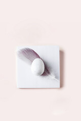 Aesthetic Happy easter card. Top view of  white egg and feather on the geometric podium.