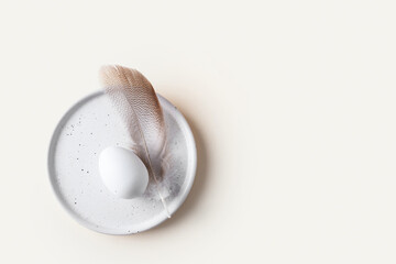 Aesthetic Happy easter concept. Top view of white egg and feather on the plate on beige background.