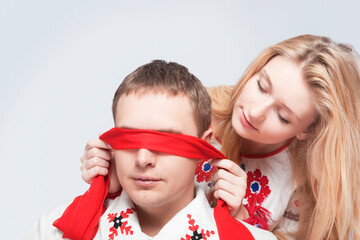 Two Loving Embraced Caucasian Couple in National Belarussian and Russian Decorated Costumes Playing With red Ribbon Against White Background.