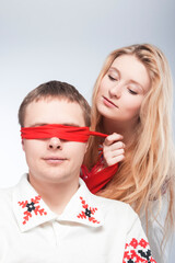 Two Loving Embraced Caucasian Couple in National Belarussian and Russian Decorated Costumes Playing With red Ribbon Blind Against White.
