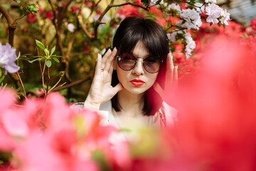 Girl in sunglasses and cream dress in a garden of azaleas