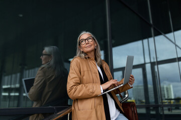 Fototapeta na wymiar portrait of successful mature adult female boss standing with laptop in the street