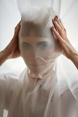 Woman portrait pulling fabric over face hiding face like a mask. Mysterious closeup portrait background of female human face under beautiful pearl silver supplex stretch fabric white vertical picture