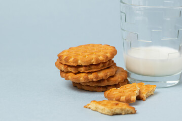 A half-empty glass of milk and a stack of cookies on a blue plain background