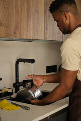 Young black man hand washing stainless steel pot with soap.
