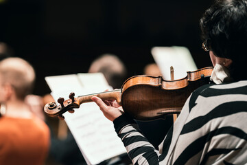 A musician playing the violin in a string section of a classical symphony orchestra rehearsal