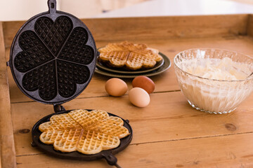 An antique waffle iron with a freshly baked waffle next to it are country eggs and a dish with freshly baked waffles