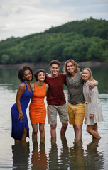 Multiracial group of young friends holding hands and standing in lake in summer.