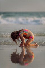 Naklejka premium Little girl looking for shells on the beach, enjoying exotic vacation.