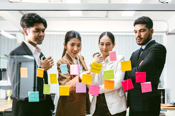 Group of successful Asian businessmen teamwork. Brainstorm meeting with sticky paper notes on the glass wall for new ideas. Using agile methodology for business in a tech start-up office.