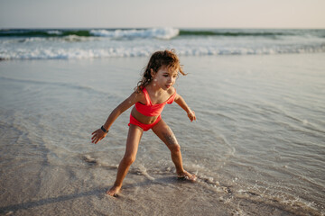 Little girl in swimsuit playing on the beach, enjoying holiday.