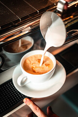 Delicious cappuccino in the making in coffee machine with milk pouring for creating foam