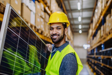 Smiling warehouse worker carring a solar panel.