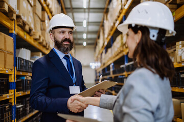 Managers in suits shaking hands in warehouse. - obrazy, fototapety, plakaty