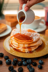Honey syrup over delicious breakfast pancakes and breakfast coffee in wooden table with plants and decoration