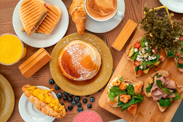 Delicious breakfast buffet with pancakes, egg croissants and coffee in wooden table with plants and decoration