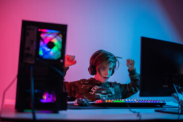 Child Playing Computer Game in Dark Room with Red LED Lights On. Preteen Boy Looking at Computer Screen While Playing Video Game Alone in Dark Room at Night.