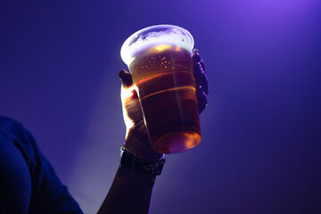 Person holding a plastic cup of beer in the nightclub.