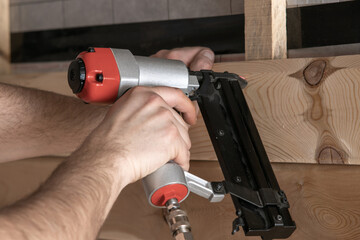 Closeup cropped male hands use pneumatic nailer, stapler nail gun for wooden plank and board....