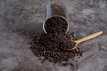 Himalayan black salt, Indian black salt or Kala namak in glass jar and wooden spoon on black stone table. Used in cooking, especially in Asian and Indian cuisine. Bath salt spa.