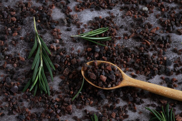 Top view of Himalayan black salt, Indian black salt or Kala namak in wooden spoon with rosemary on  on black stone table. Flat lay out.