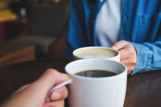 Closeup image of a couple people clinking white coffee mugs in cafe