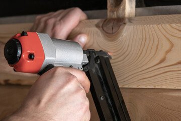 Close up cropped carpenter male hands use pneumatic nailer, stapler gun for wood timber plank....