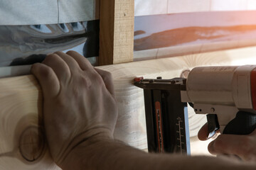 Cropped builder hands holding pneumatic nail gun, stapler for wooden board. Scoring, set up metal...