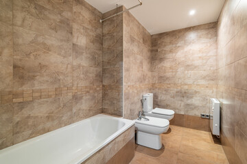 Naklejka na ściany i meble Spacious bathroom with beige brown tiles, bathroom with toilet and bidet. The concept of a stylish and simple renovation in your apartment or hotel. Copyspace