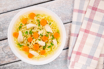 Homemade chicken soup with noodles and vegetables in a white bowl, on a wooden background.