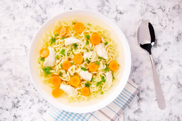 Homemade chicken soup with noodles and vegetables in a white bowl, on a gray background.