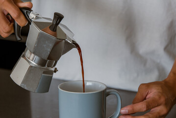 Hand pouring coffee from bialetti coffee pot into mug
