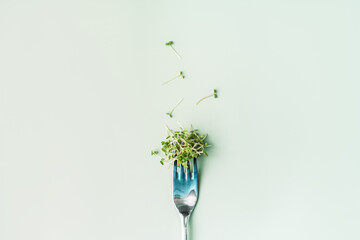 Young sprouts of microgreens on fork on green background.