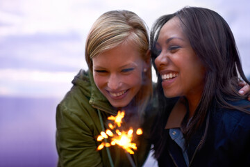Making special holiday memories. Two young women standing with sparklers with the twilight sky...
