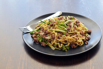 Stir fry noodles with minced beef, spring onion and chillies on a black plate. Spicy noodles on the table. 