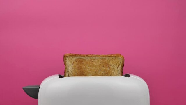 Fried toast bread pops out of a white modern toaster on a pink background, slow motion