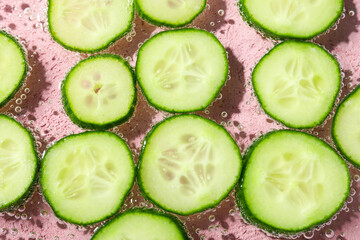 Slices of cucumber in water on pink background