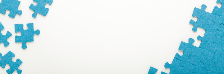 Different many blue puzzle pieces on white table background. Closeup. Top down view. Jigsaw wide banner. Empty place for text.