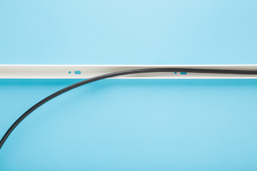 Dark black new wire in white plastic channel on light blue table background. Pastel color. Closeup. Wiring installation. Top down view.