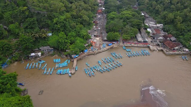 Aerial view of fisherman boats anchored on the harbour with brown sea water. The boats are blue - Orbit drone shot