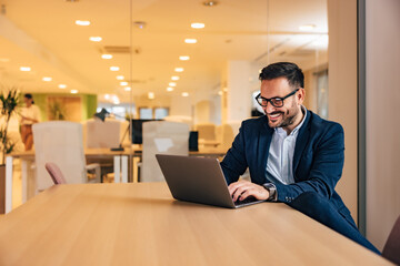 Smiling businessman chatting online with clients, using a laptop, sitting at the office.