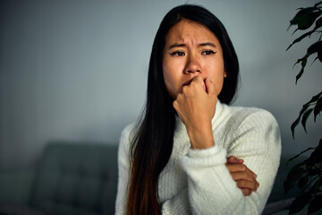 Fototapeta na wymiar A sad Asian woman is crying while sitting alone on the couch at home.